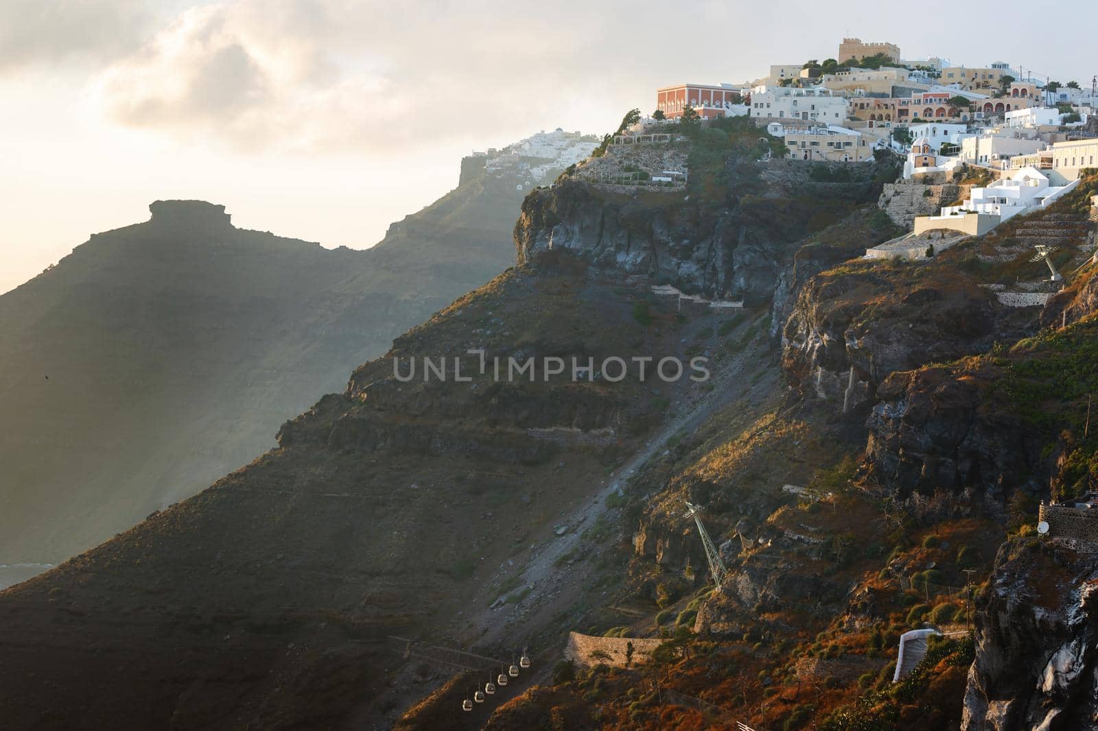 Sunset on the Greek Island of Santorini,with colorful  warm light and clouds over the town. The view follows the edge of the caldera from Thira, Skaros rock,  Imerovigli and Oia towards the sun