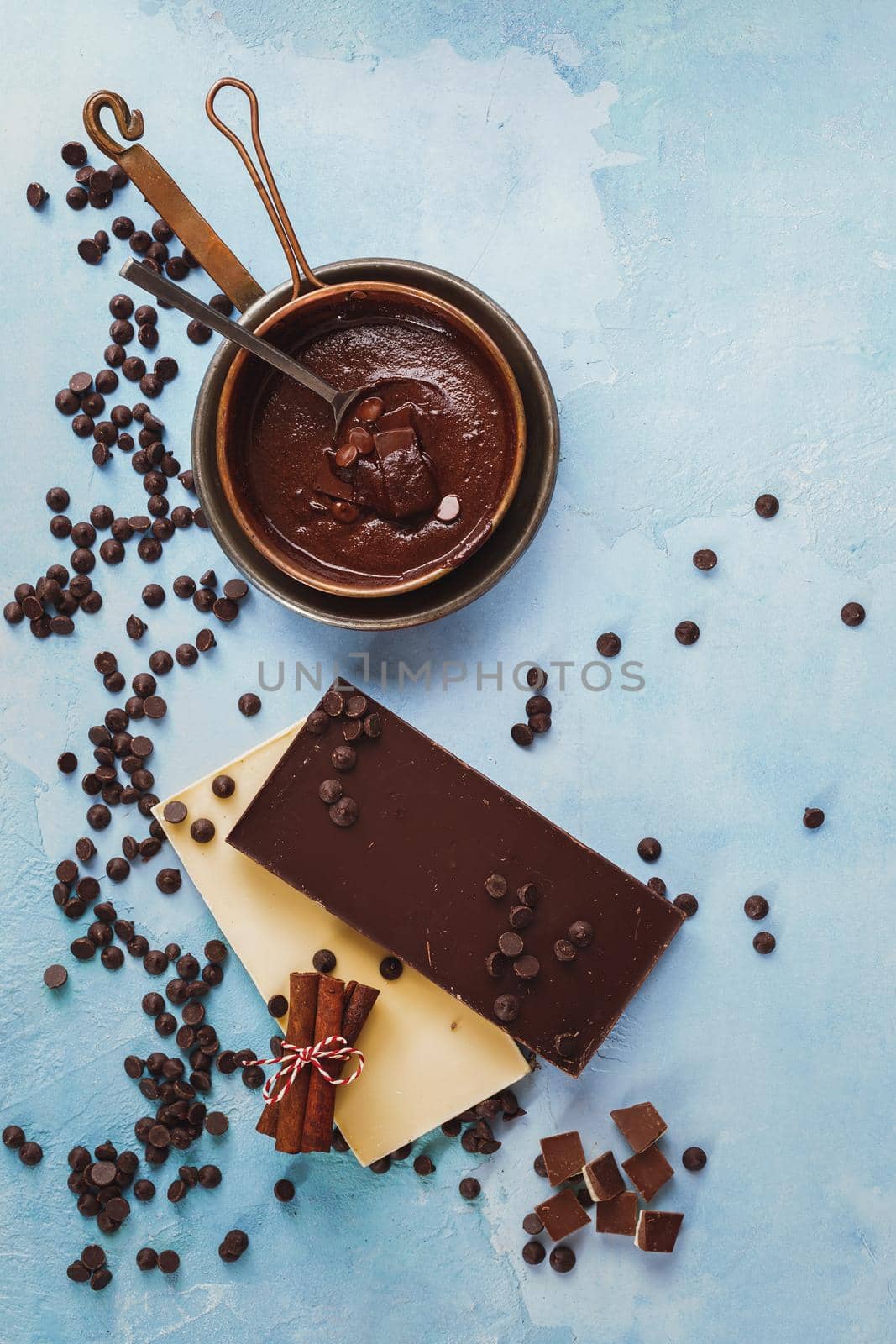 Melted chocolate in copper pan and  bars of dark and white chocolate beside on rustic blue surface by Slast20