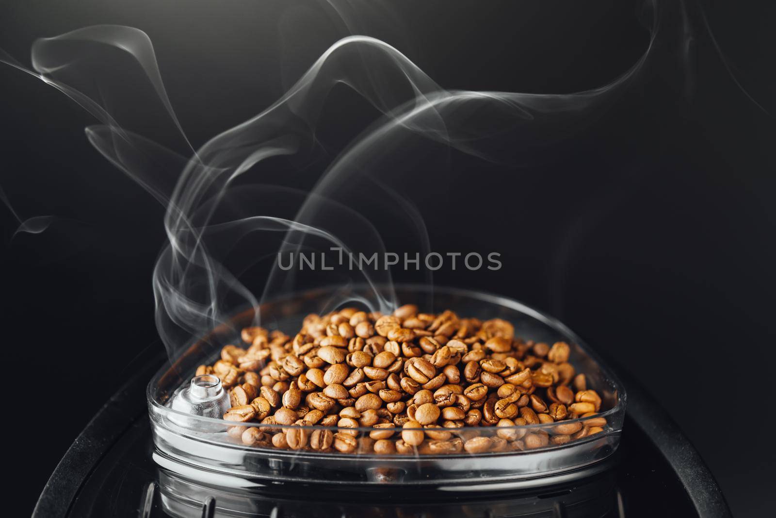 fresh roasted coffee beans with smoke in coffeemaker bean container, close-up view