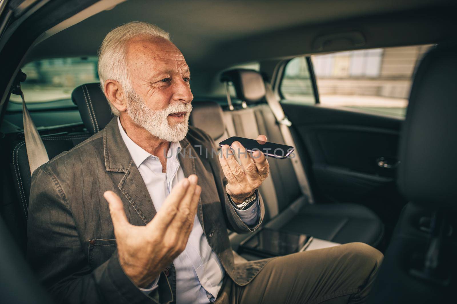Shot of a successful senior businessman making voice message on his smartphone while sitting in the backseat of a car during his morning commute.