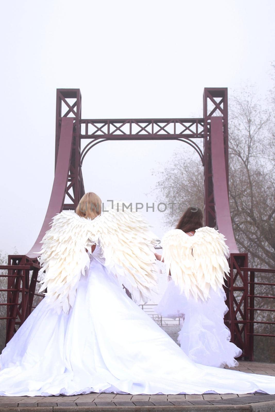 Two girls in angel costumes and white dresses walking in the park. Mother and daughter