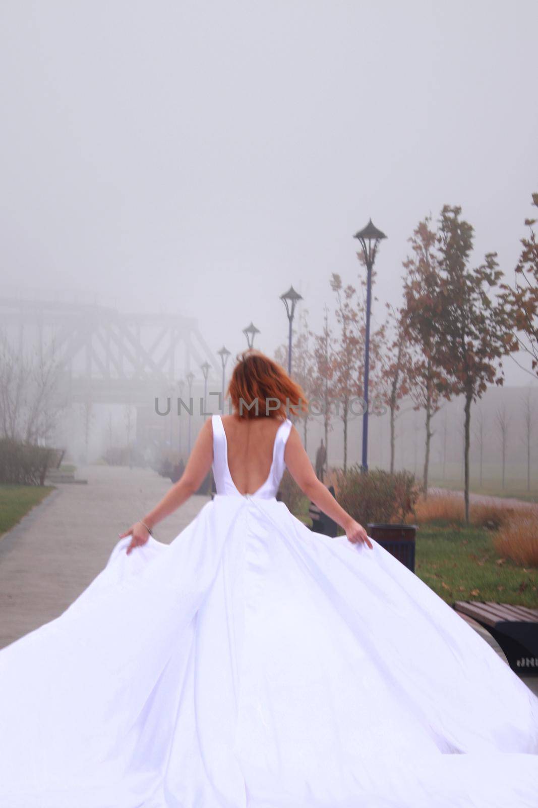 A redhead women in a white dress. A bride. Running away in the park