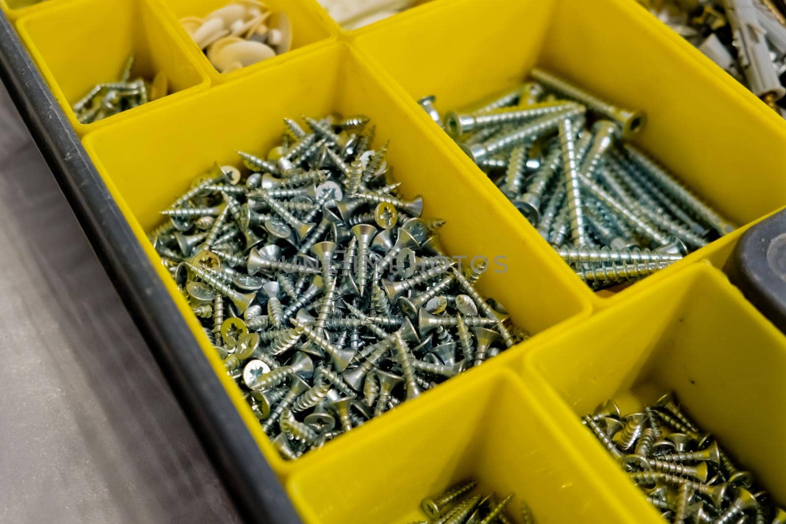 Close-up of small plastic yellow boxes with different screws and fasteners. Selective focus.