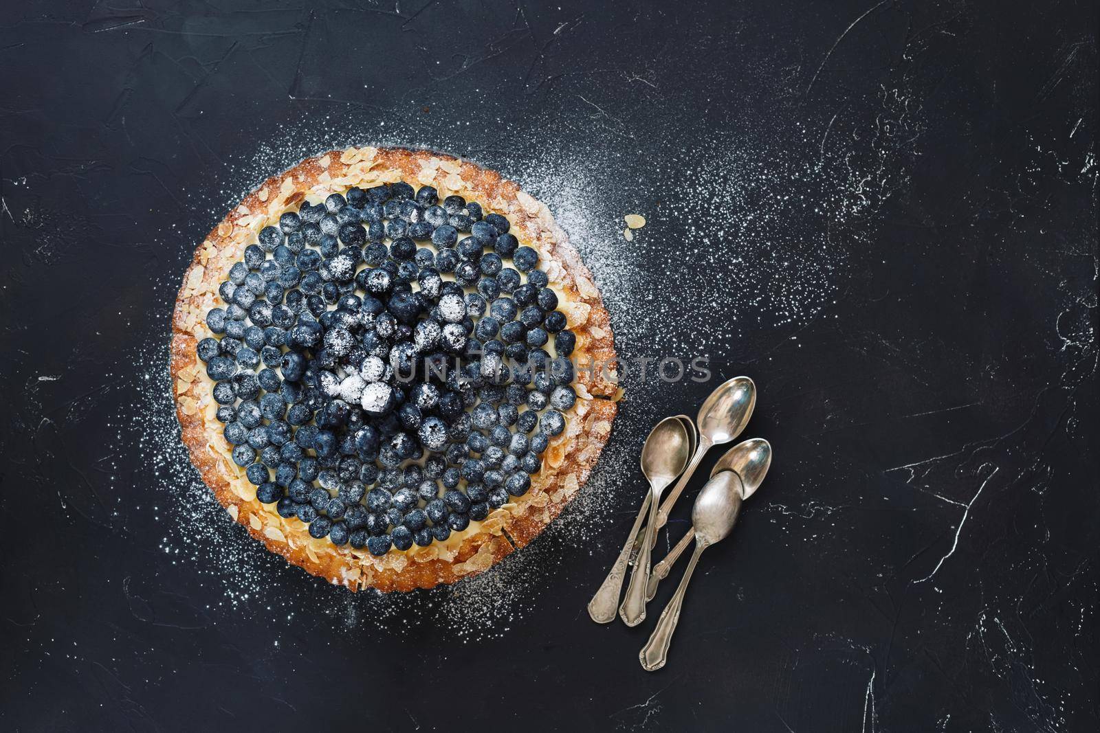 Delicious homemade blueberry almond tart with fresh blueberries and bunch of teaspoons beside. Top  view, blank space, dark toned image by Slast20