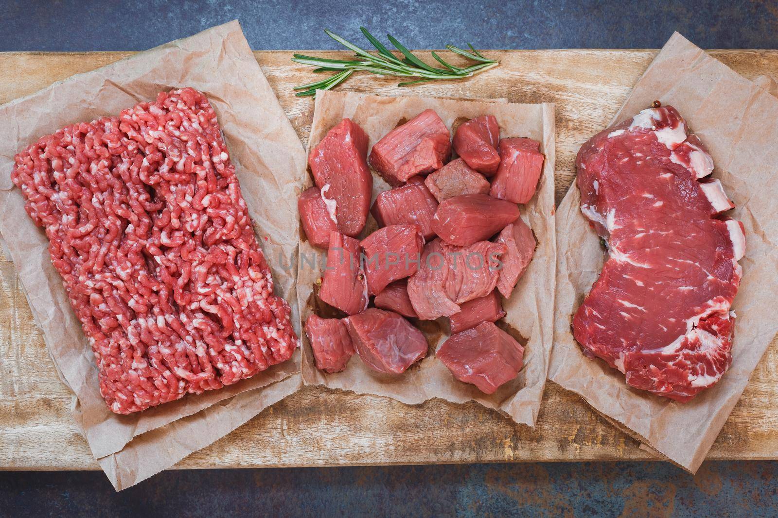 Fresh raw angus beef meat, whole, ground and chopped on parchment paper , wooden cutting board,  stone background, top view by Slast20