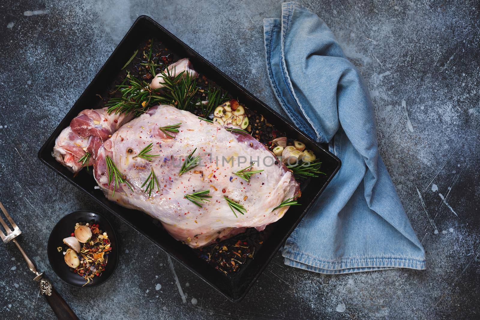 Leg of lamb studded with rosemary in roasting tin.  Traditional Easter and Christmas meal, top view, blank space