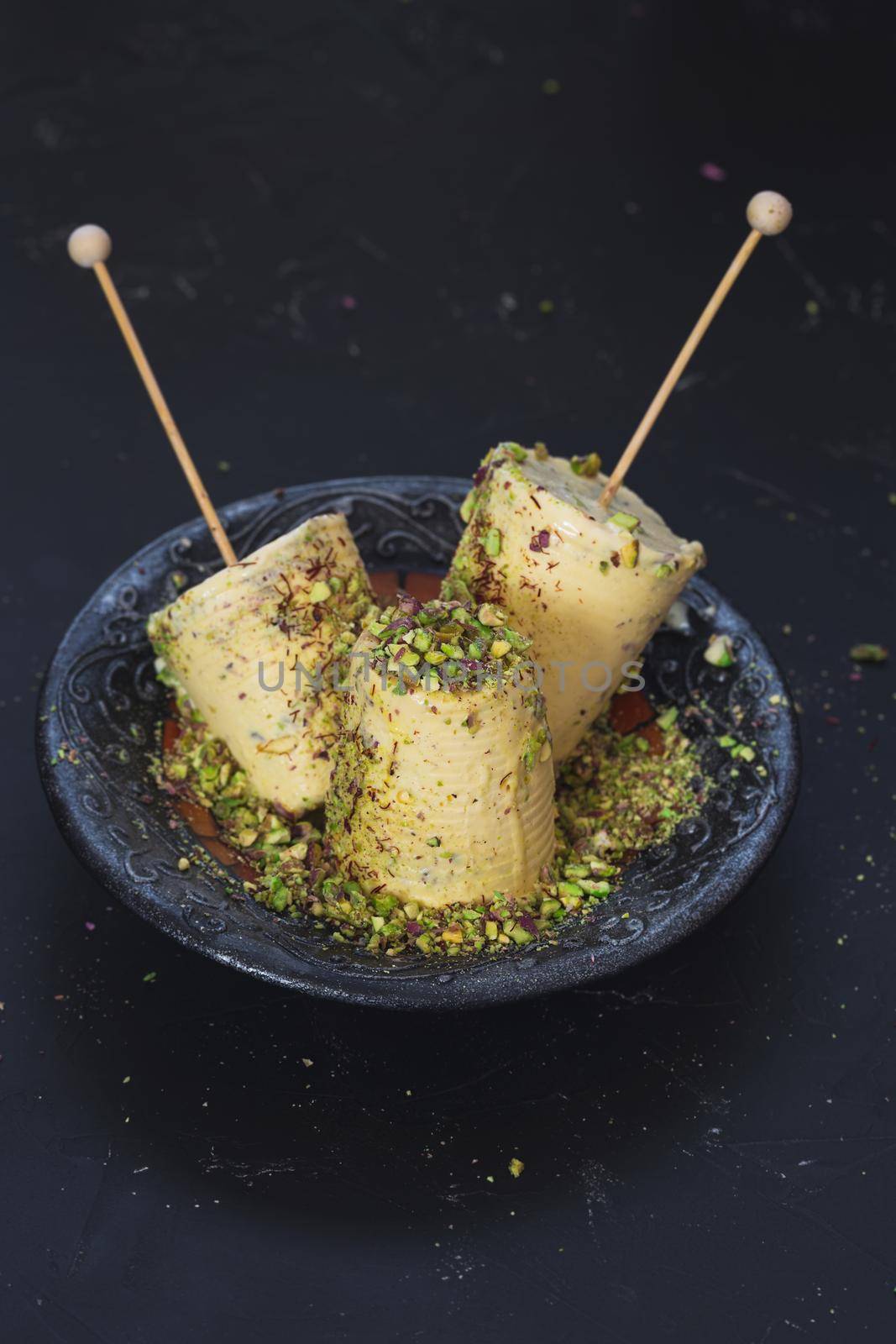 Pistachio and Saffron Kulfi, traditional Indian dessert on dark surface, ready to eat.  Selective focus, blank space