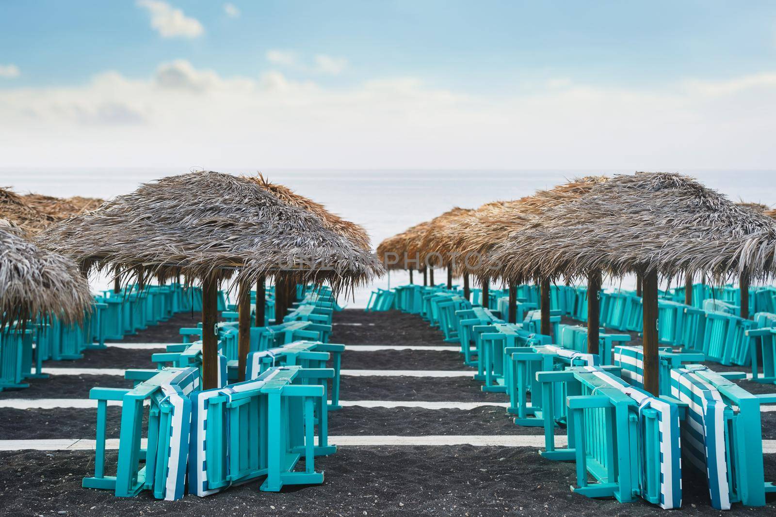 Perissa Black Sand Beach, Santorini, Greece in the morning. Beachside thatched umbrella and beach beds with a sea view by Slast20
