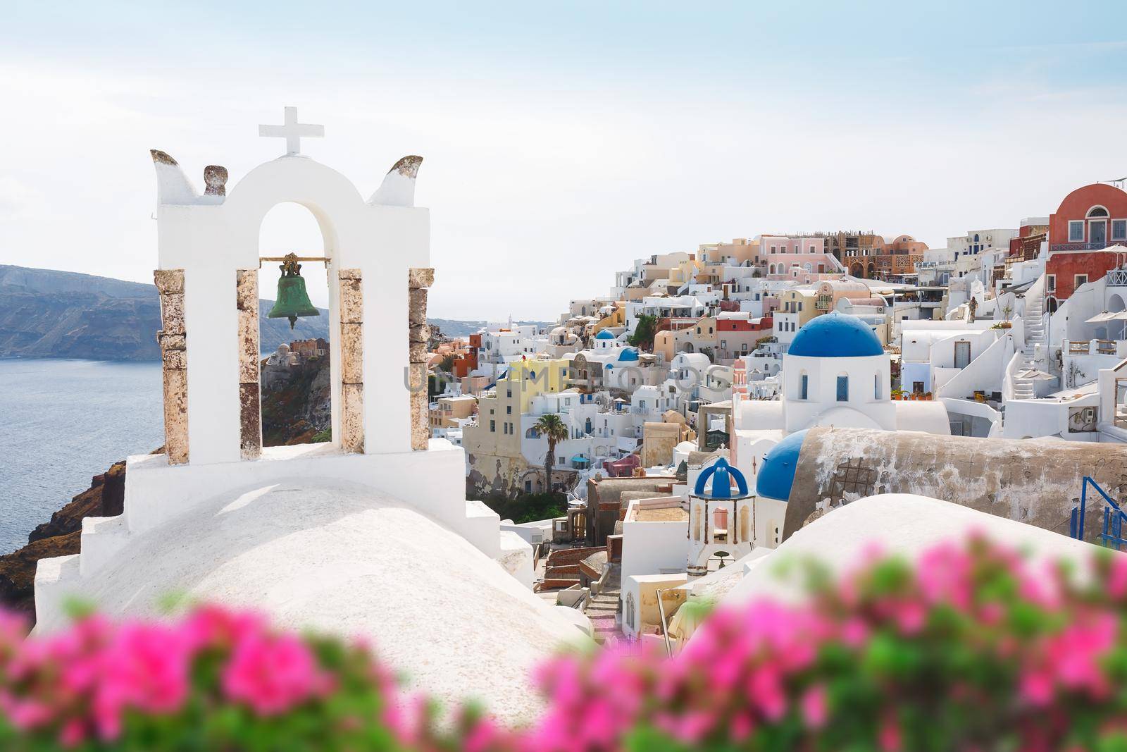 Oia village  through flowers and  traditional Greek white church arch with cross and bells in Oia village of Cyclades Island, Santorini by Slast20