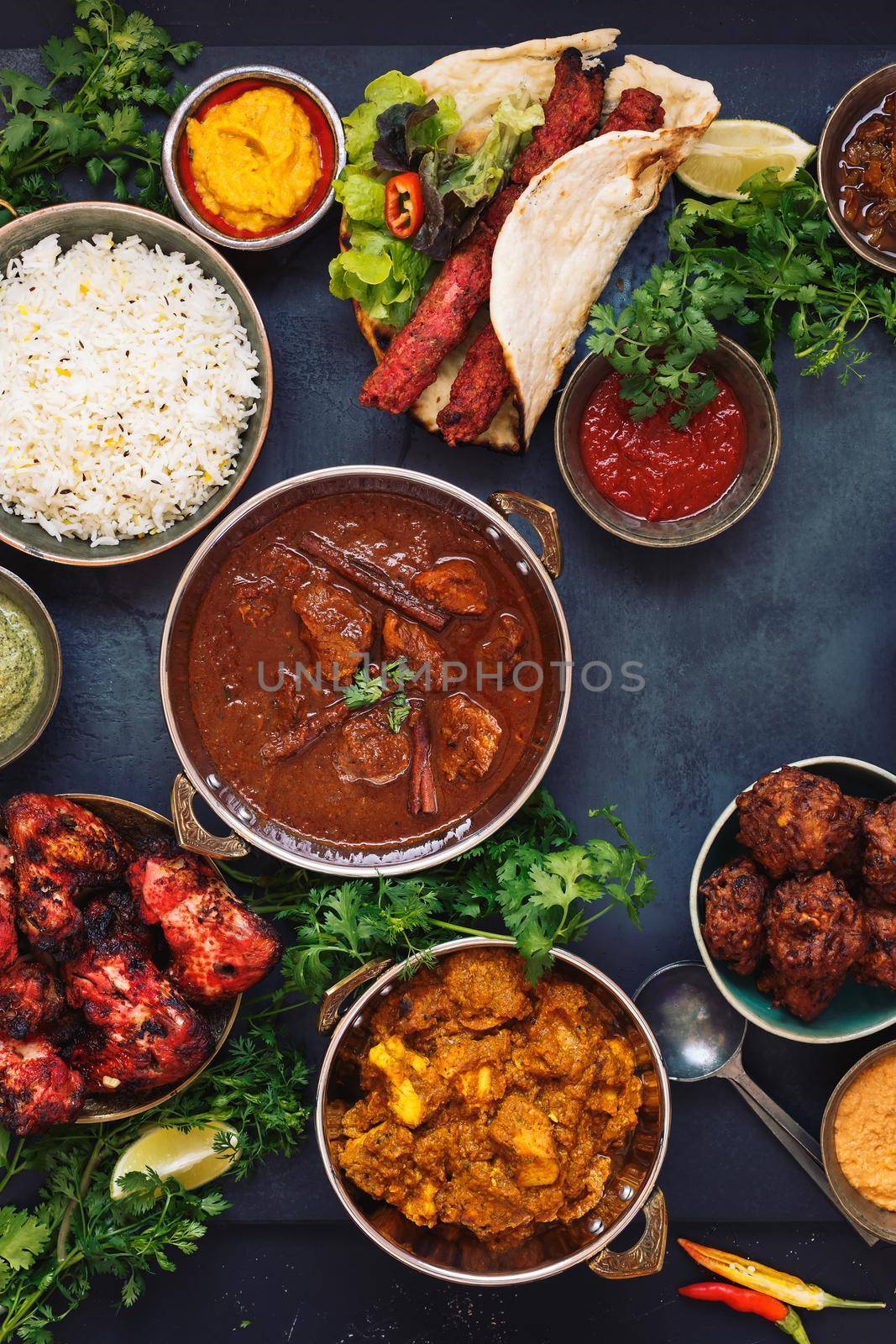 Various Indian dishes featuring  rogan josh, chicken tikka masala,tandoori chicken wings  and  kebabs, with rice and naan bread, top view