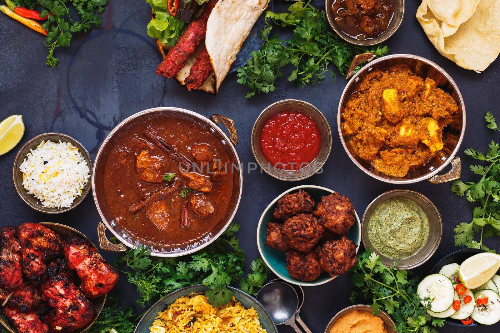 Taste of India. A selection of Indian food with various bowls of food featuring  chicken tikka masala, rogan josh, kebabs, tandoori chicken wings, pasties, poppadoms with dips and naan bread