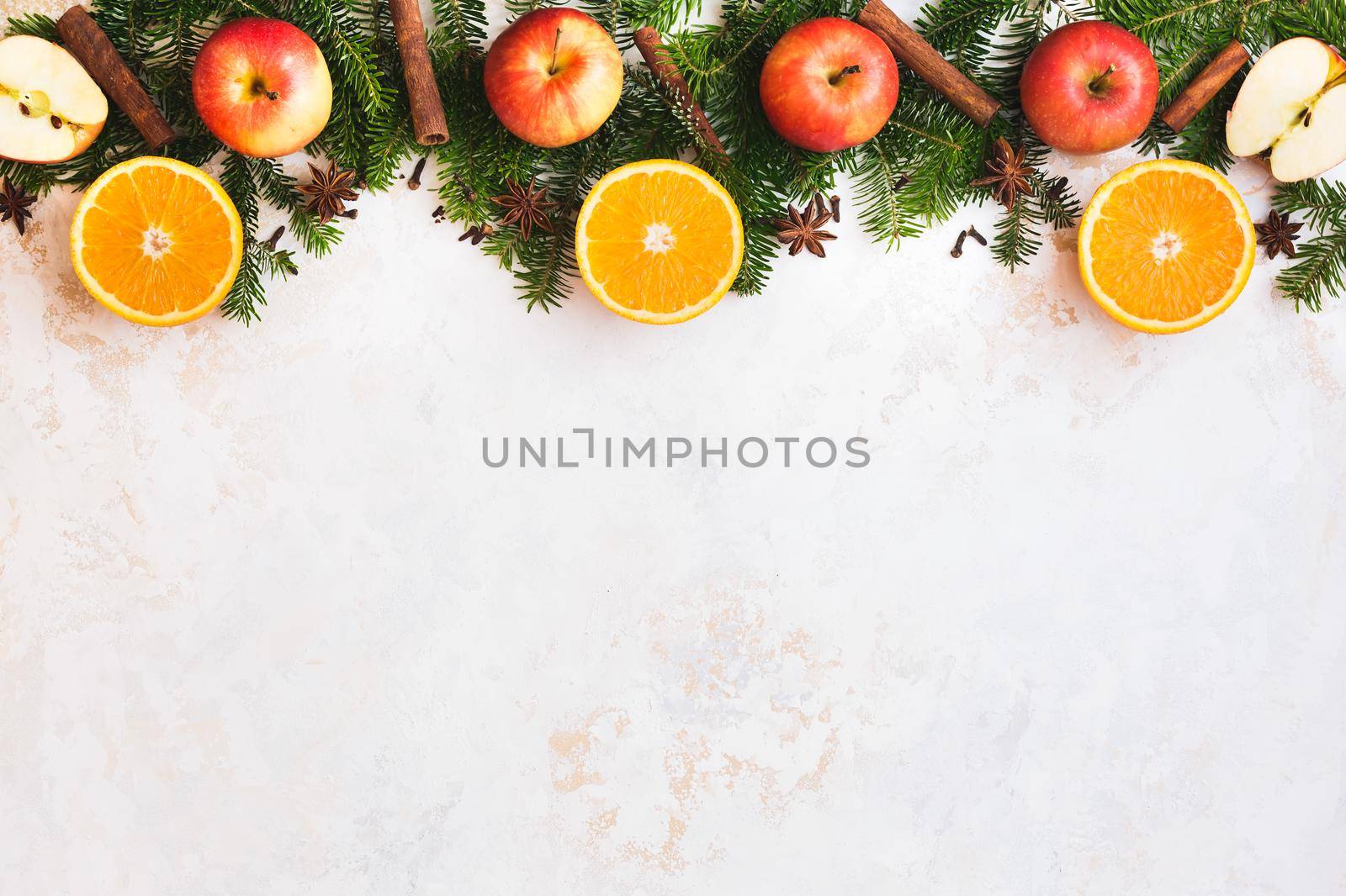 Christmas fresh  fruit abstract background border with orange half, spices, apple whole and half and natural fir tree over golden white rustic surface, top view