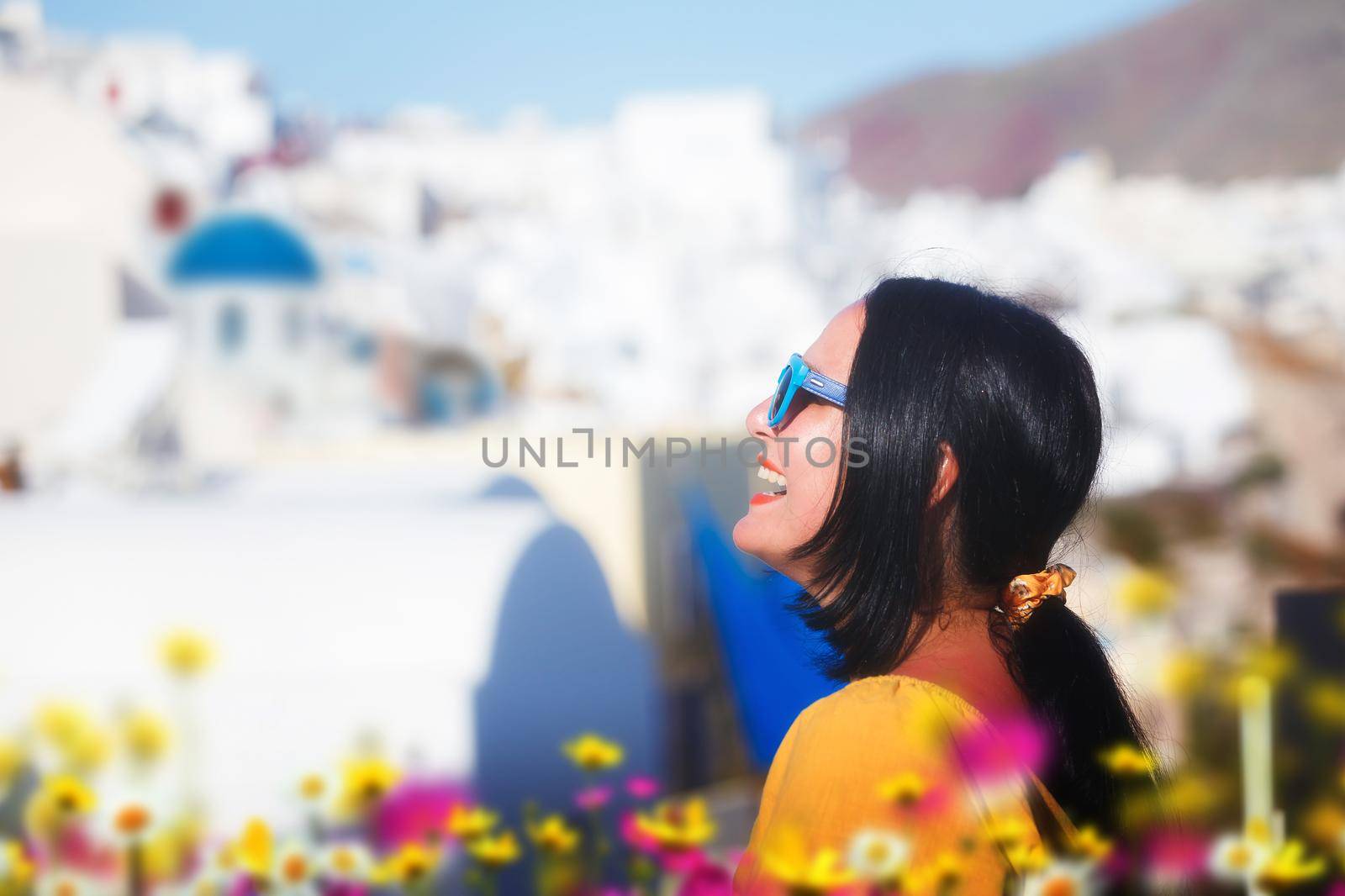 Portrait Of Smiling Young Woman Standing Against Buildings At Oia In Santorini,  Greece