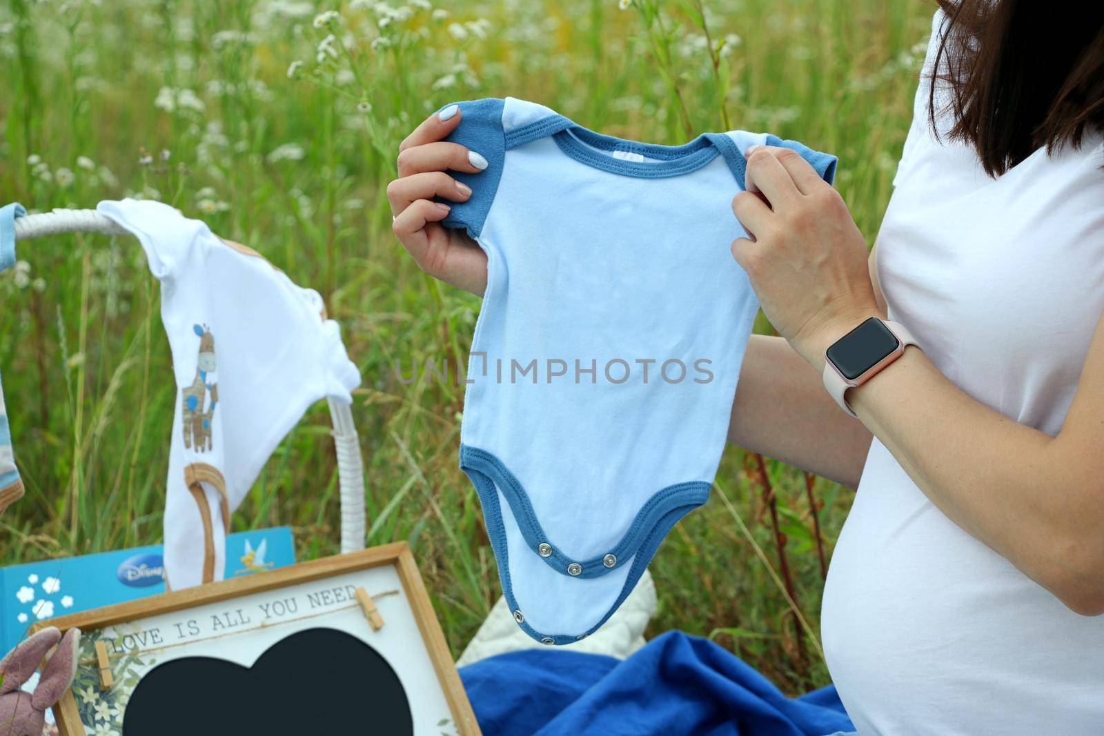 Pregnant woman in white t-shirt holding a blue baby bodysuit in the field