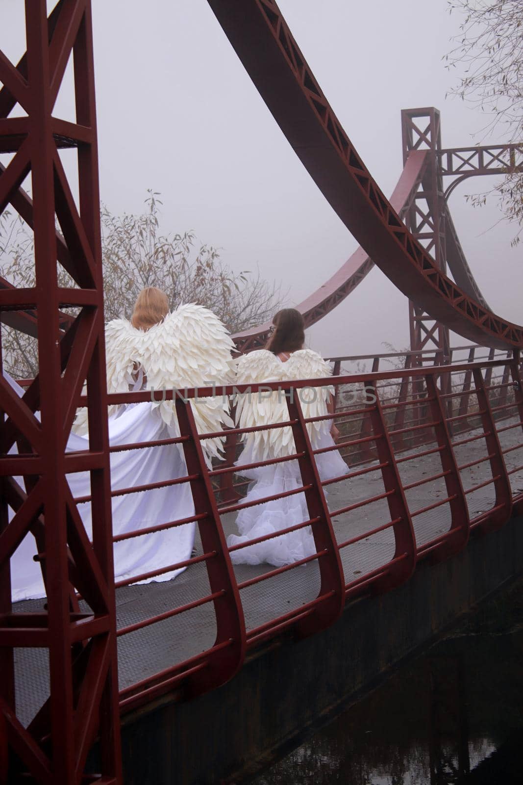 Two girls in angel costumes and white dresses walking in the park. Mother and daughter