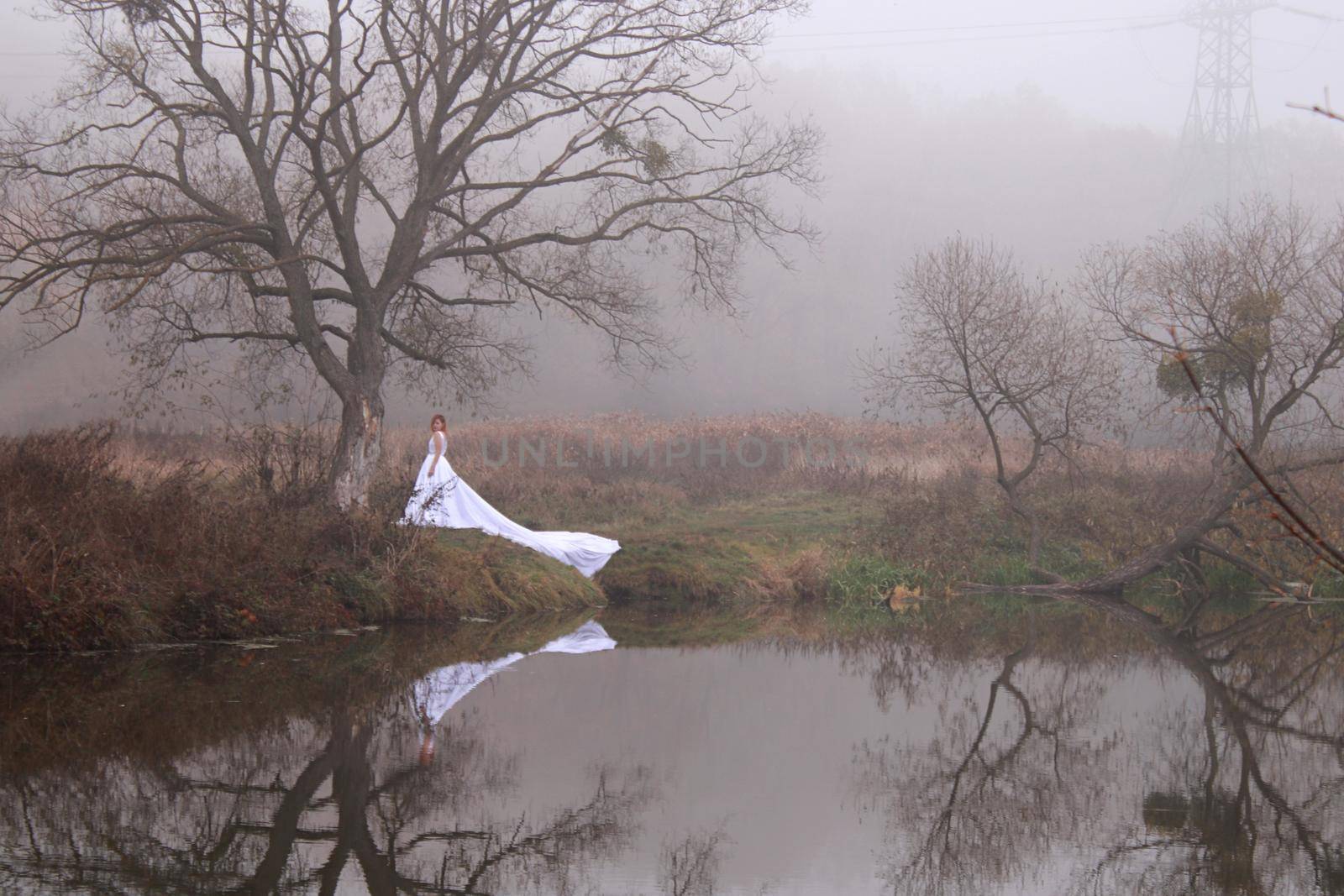 A redhead women in a white dress. A bride. in the forest near the lake