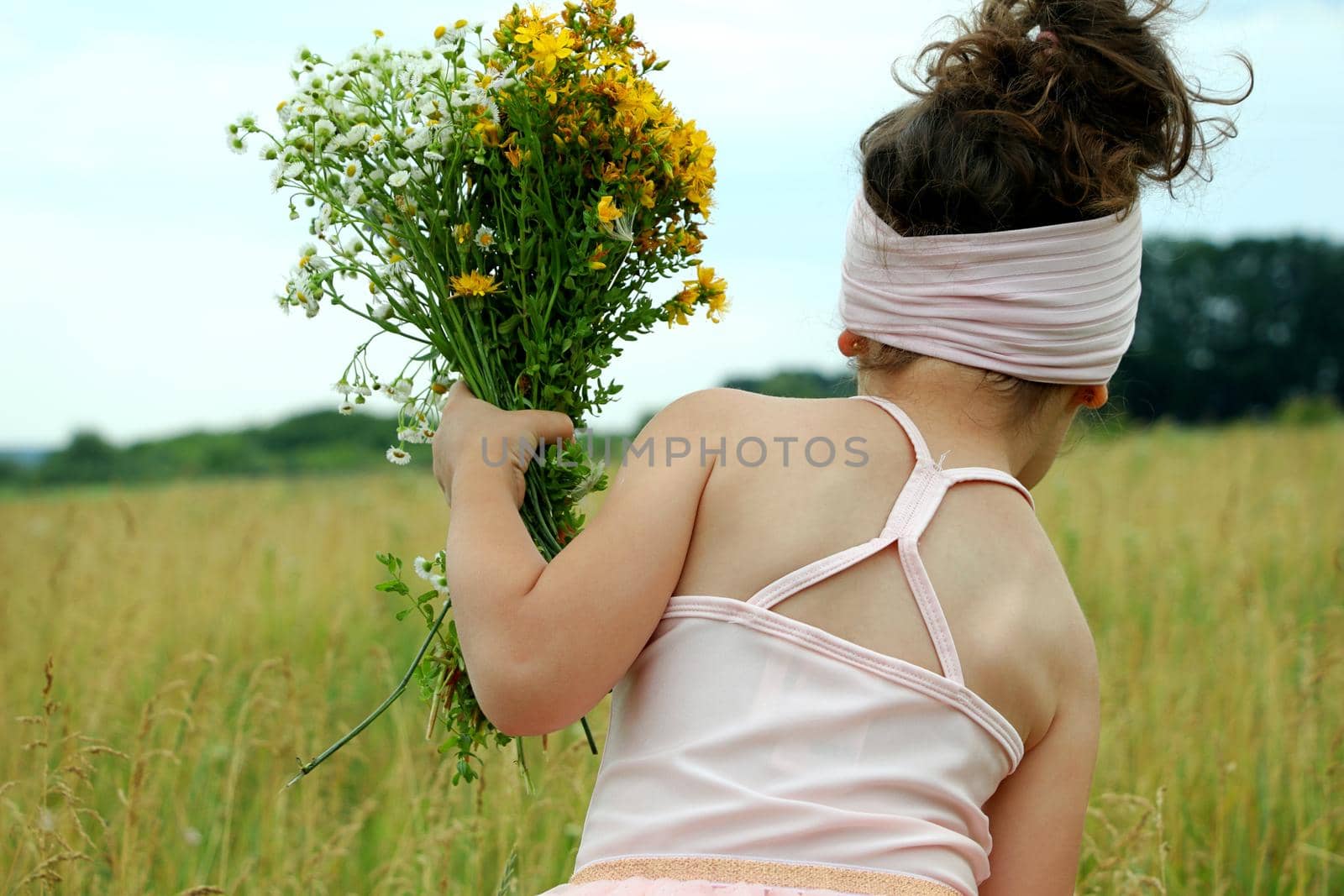 Little girl with flowers in pink dress playing in the field happy