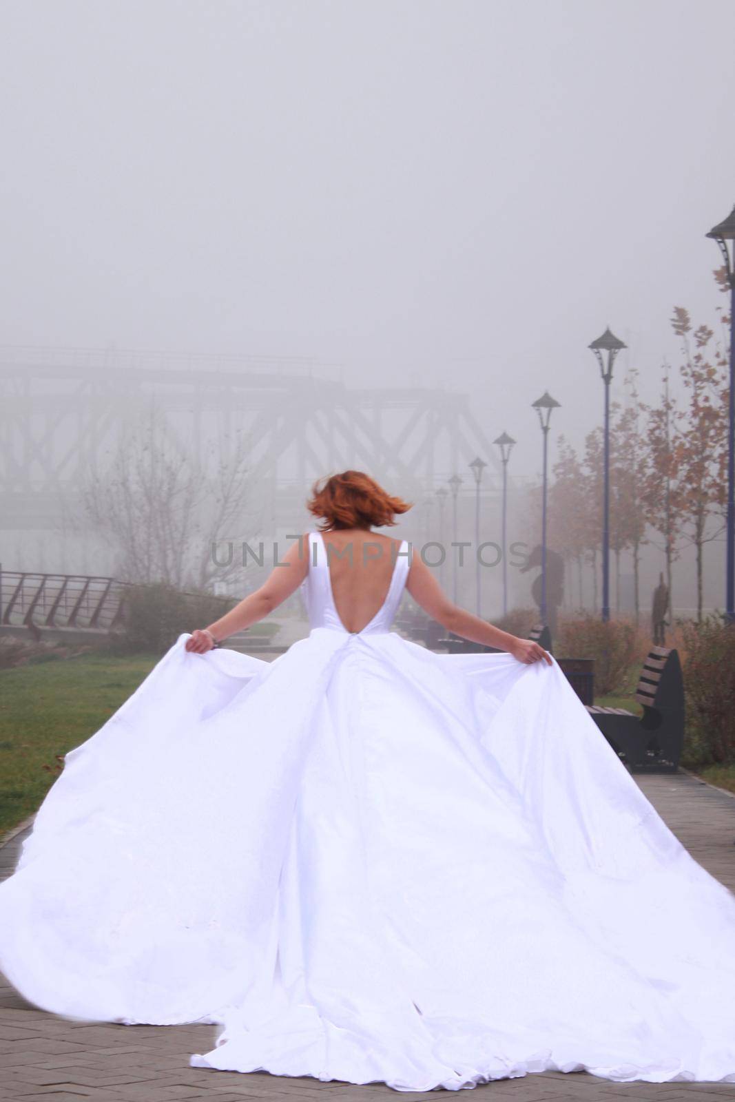 A redhead women in a white dress. A bride. Running away in the park