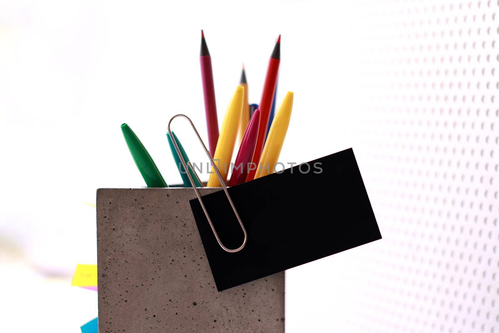 A concrete organiser with office supplies in it and a business card attached