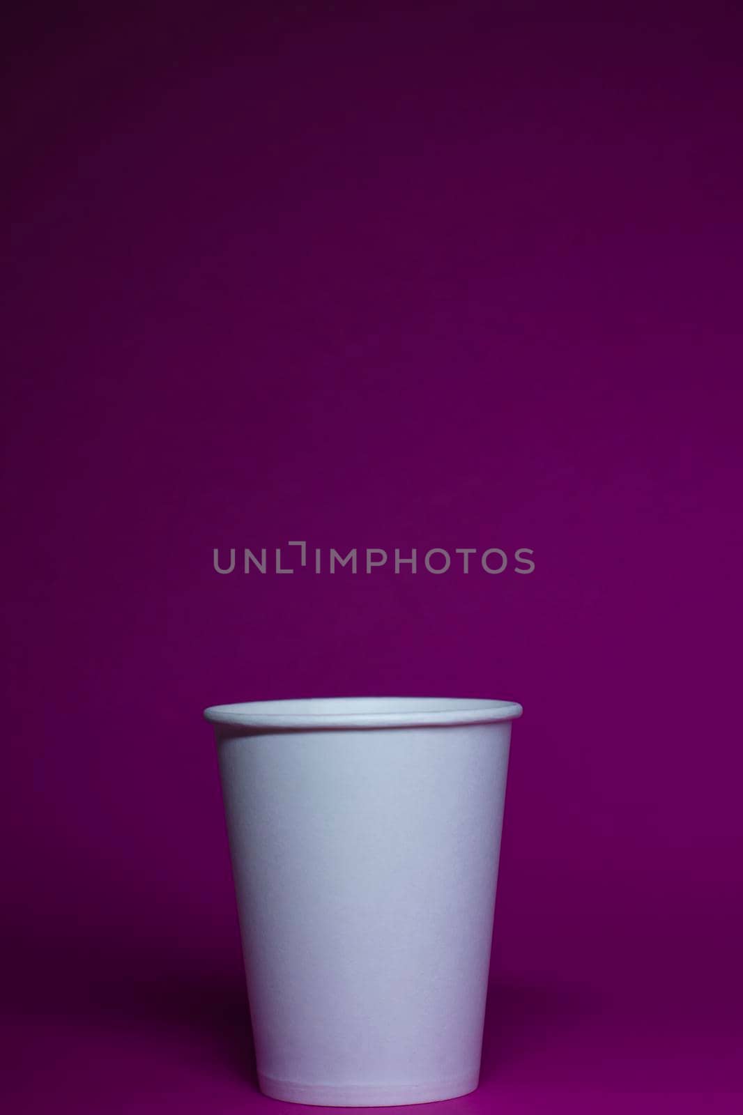 An empty white paper cup on a pink background. vertical photo.