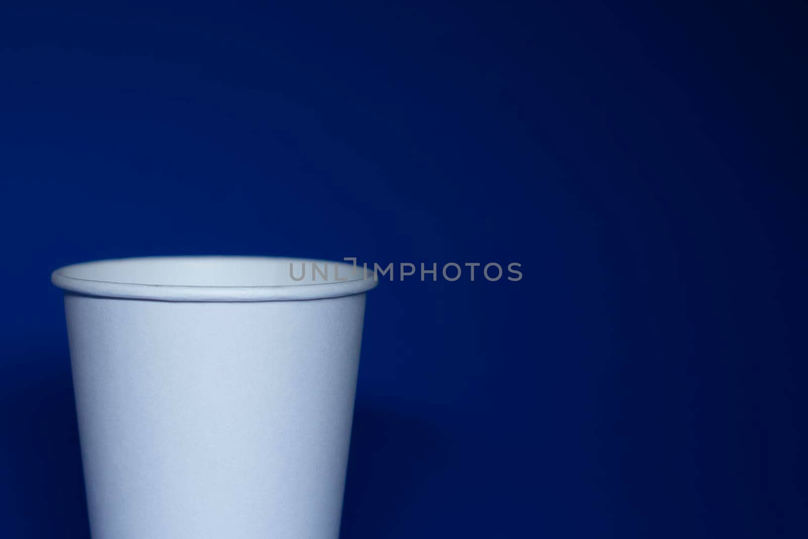 An empty white paper cup on a blue background. horizontal photo.