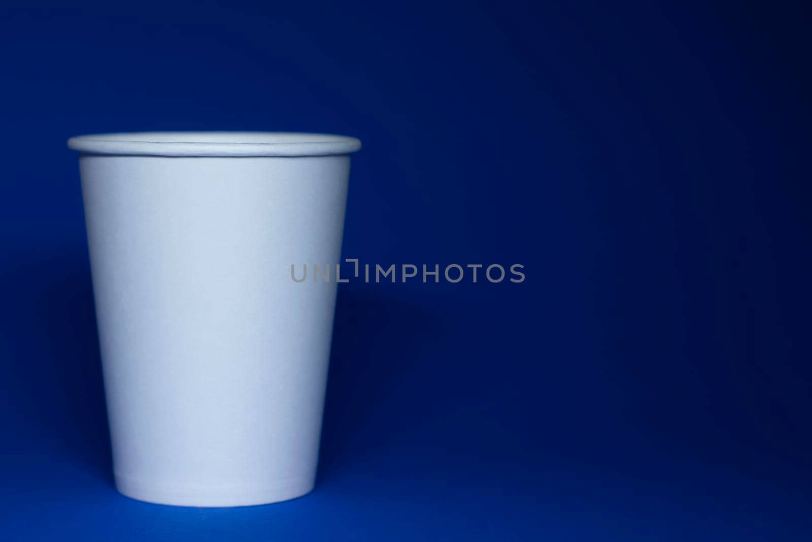 An empty white paper cup on a blue background. horizontal photo.