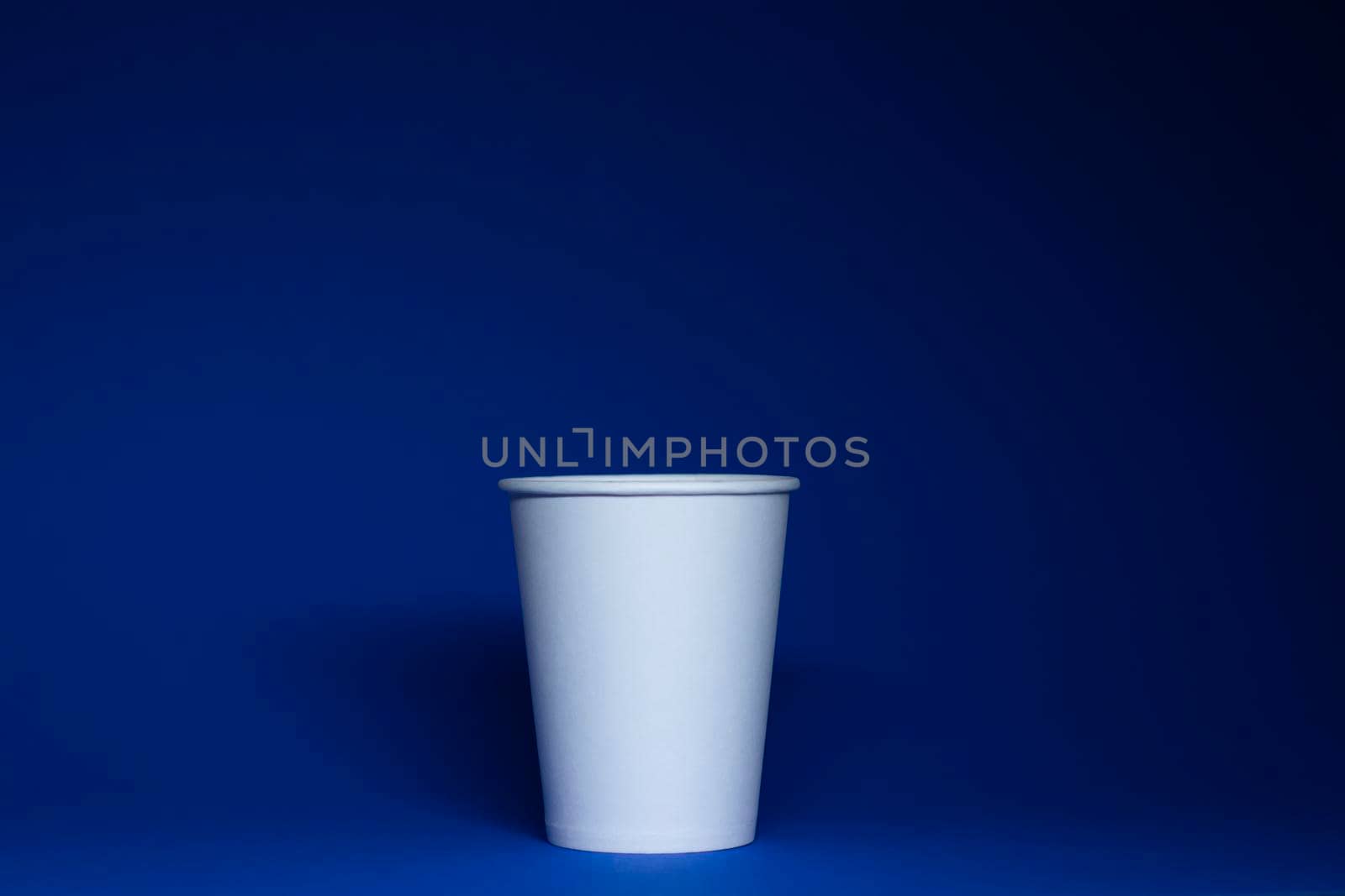 An empty white paper cup on a blue background. horizontal photo.