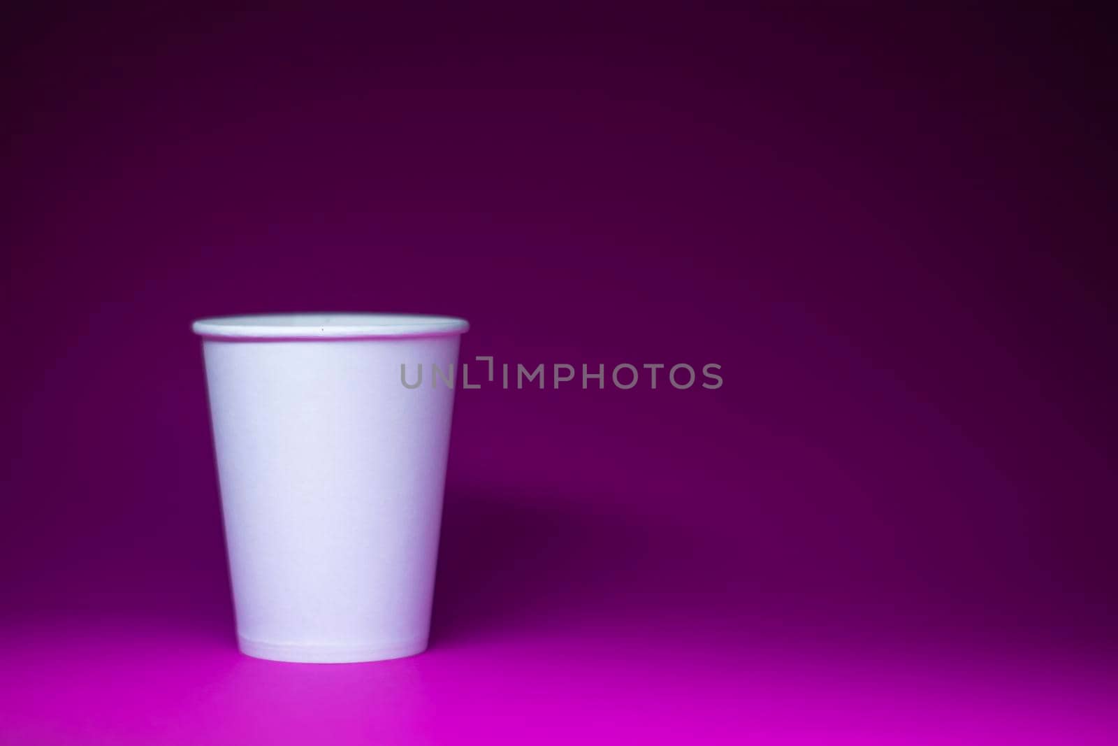 An empty white paper cup on a pink background. horizontal photo.