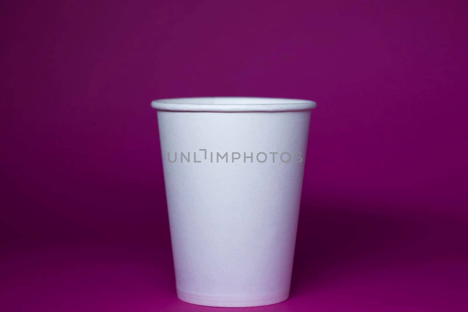 An empty white paper cup on a pink background. horizontal photo.