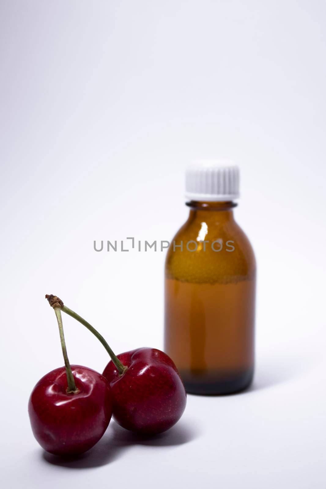 little liquid bottle with no label near cherry. body care and beauty concept. Copy space by oliavesna