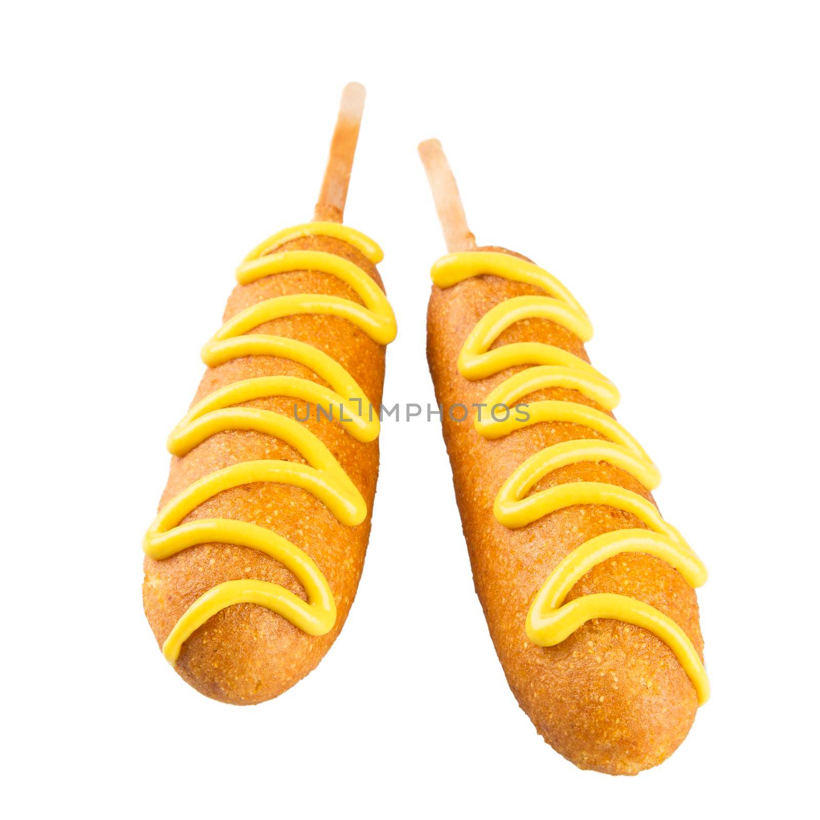 Two corn dogs isolated on a white background topped with mustard