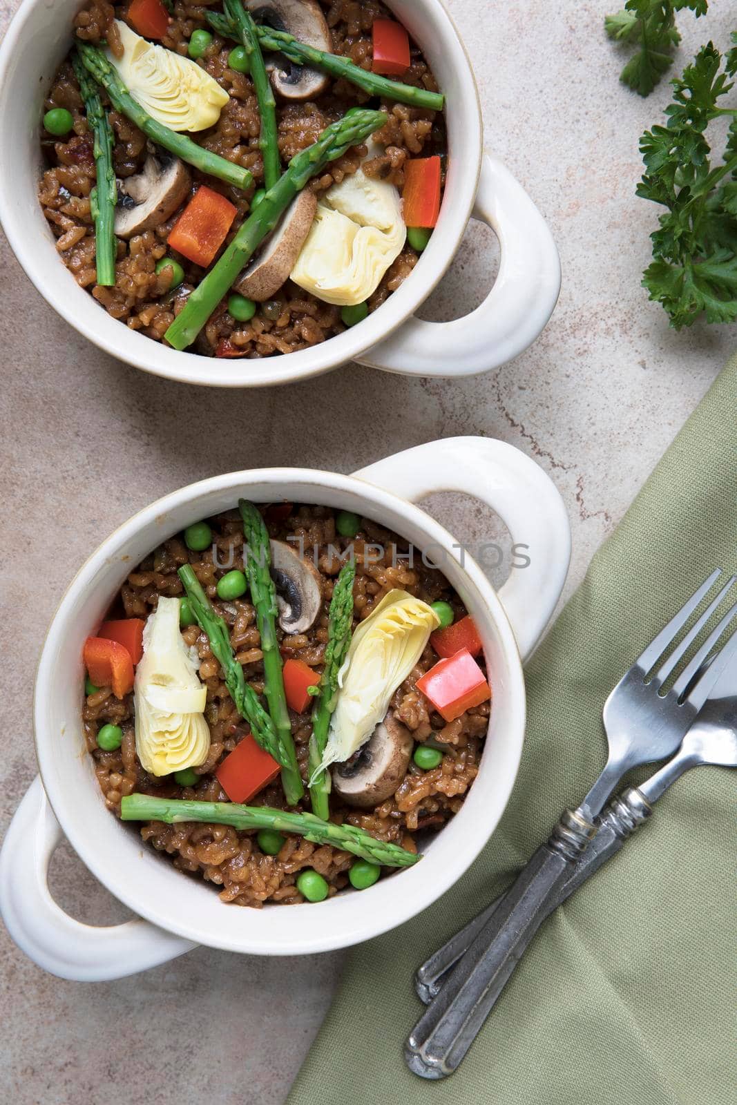 Two bowls of vegan paella with asparagus, mushrooms and artichoke hearts - flat lay.