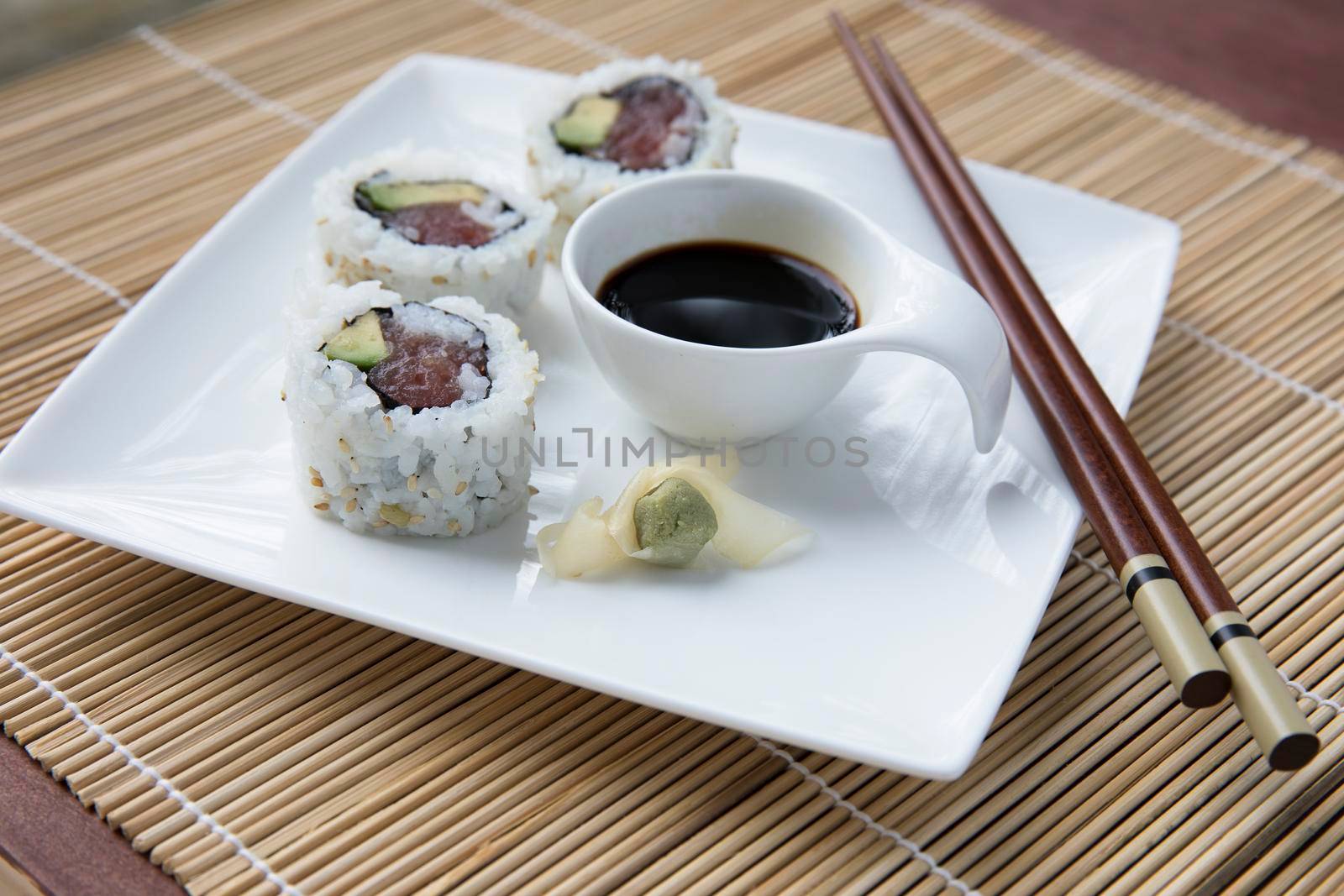 Fresh tuna and avocado uramaki sushi rolls on a white platter with soy sauce, wasabi, and chop sticks