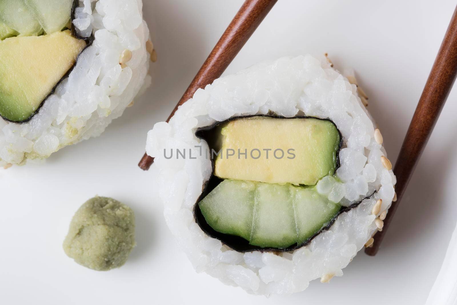 Vegan cucumber and avocado uramaki sushi rolls with wasabi and chop sticks.