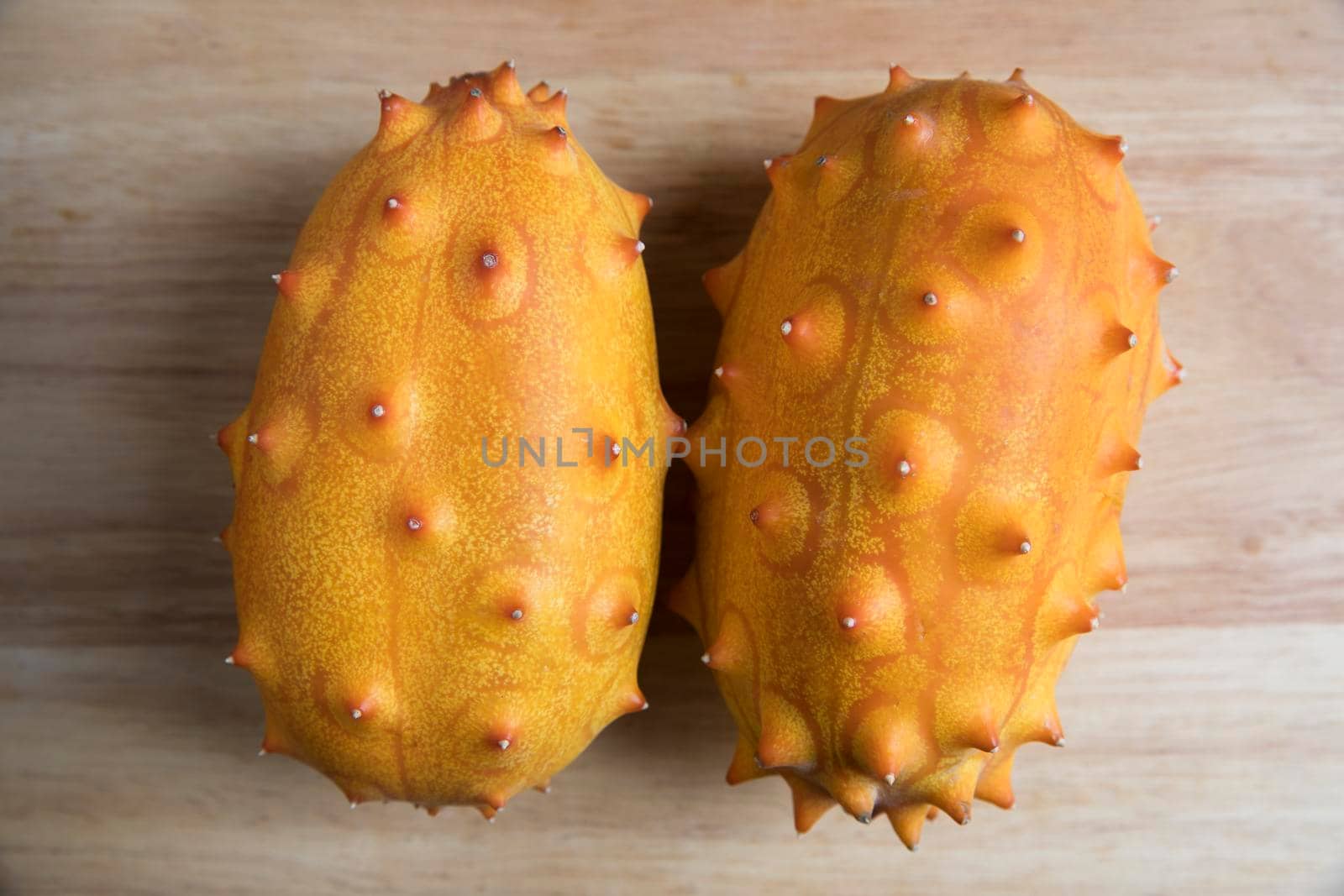 Two whole kiwano fruits on wodden surface from high angle.