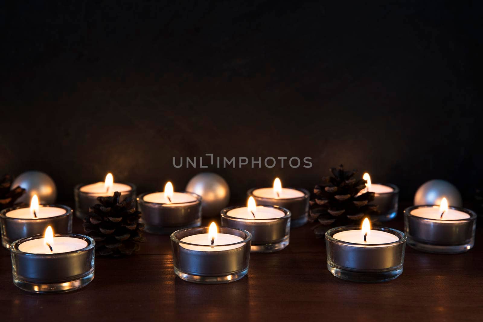 Tea lights with pine cones and baubles on a wooden surface, with copy space.