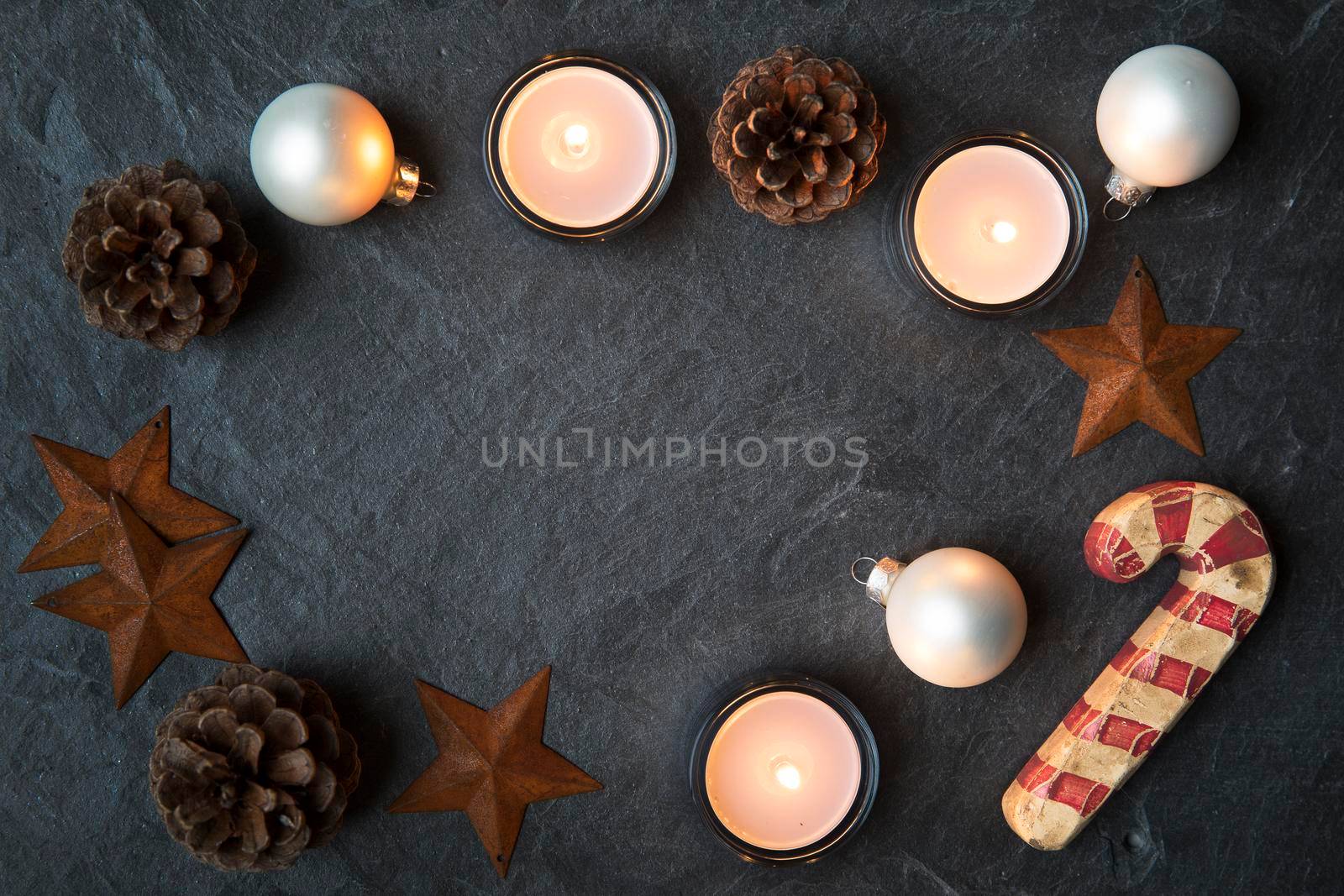 Rustic Christmas decorations and tea lights on dark stone surface with copy space in the center.  Viewed from directly above