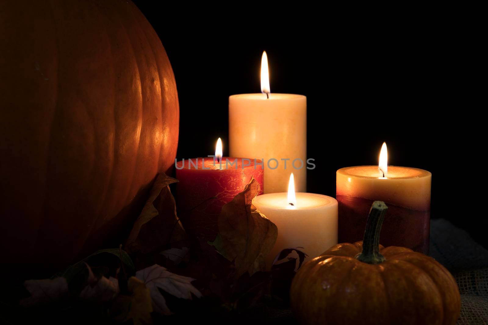 Autumn candles burning surrounded by leaves and gourds.