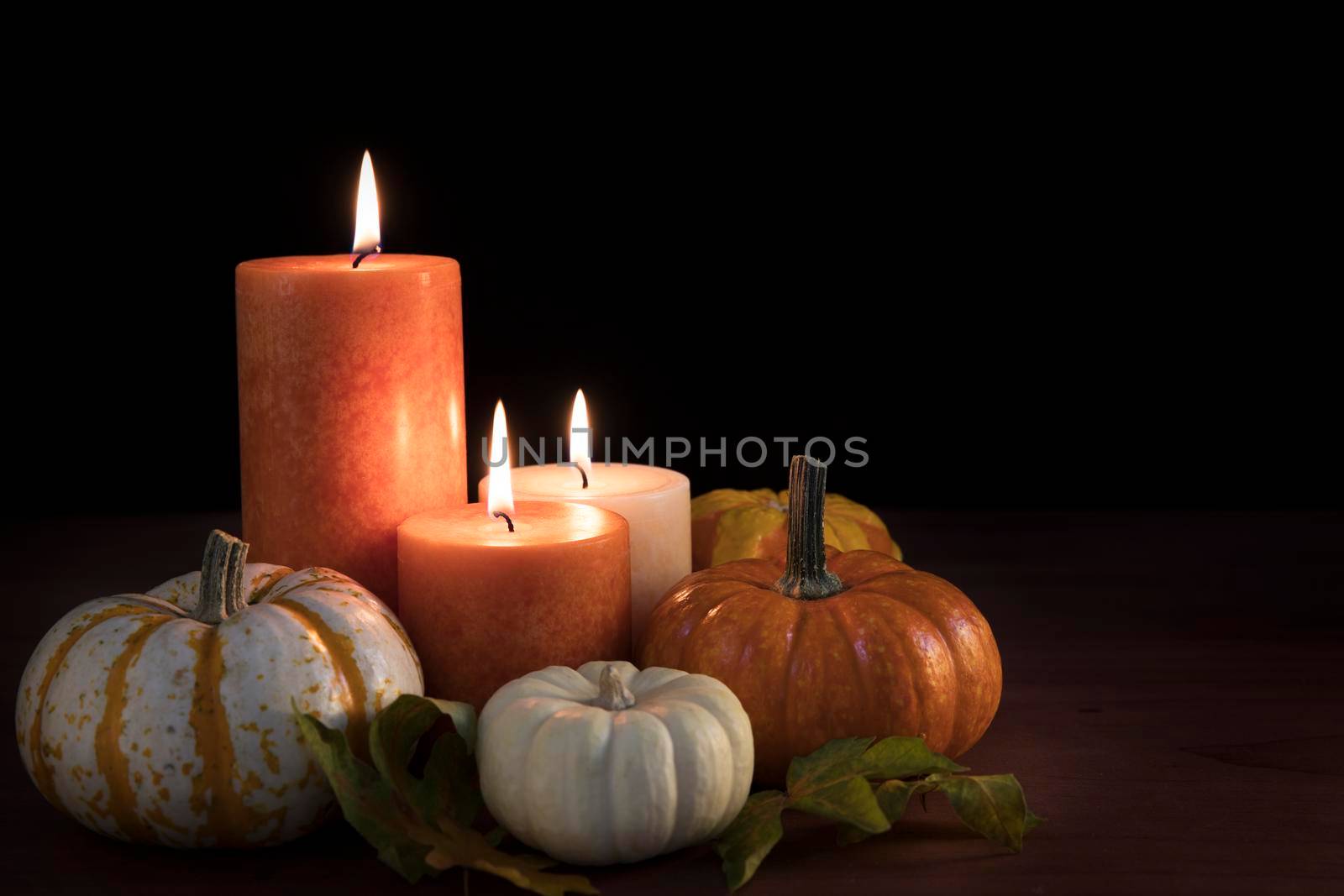 Three candles surrounded by gourds with black background and space for copy.