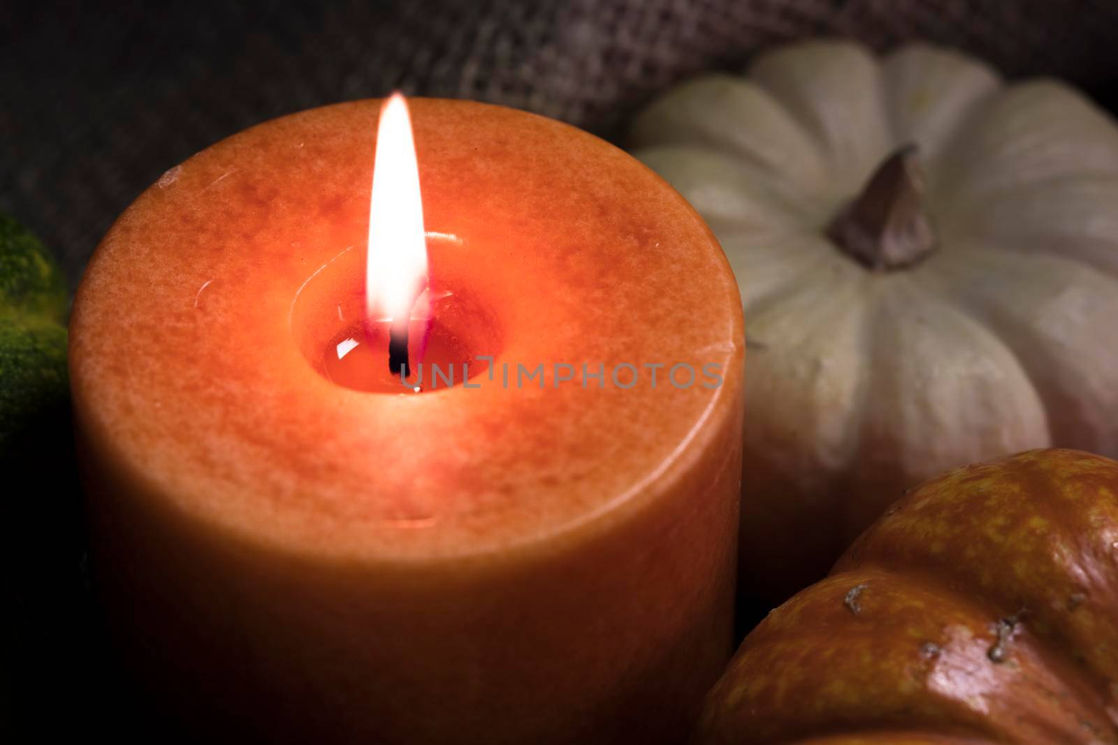 Fall theme close up of orange candle burning with gourds