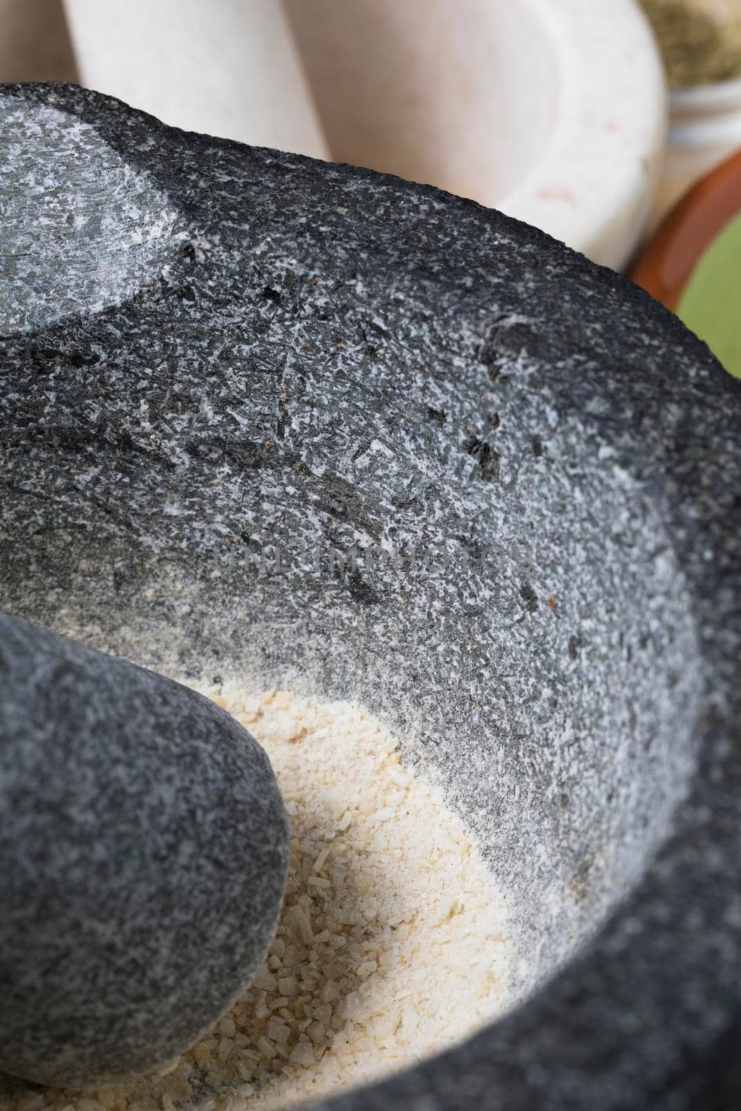 Vertical orientation close up of stone mortar and pestle with crushed dried onion.