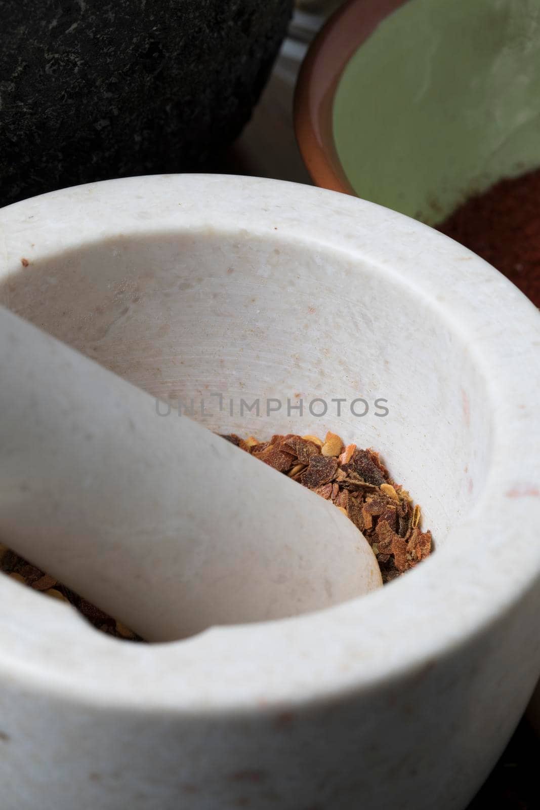 Vertical orientation close up of porcelain mortar and pestle with crushed dried chili pepper.