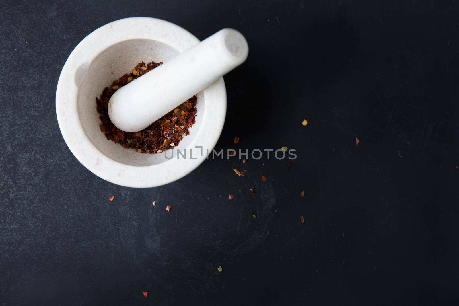 Small porcelain mortar and pestle with dried chili pepper on dark surface with copy space.