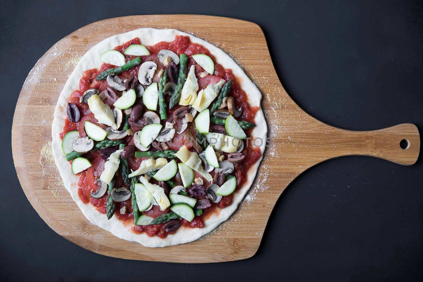 Homemade vegan pizza on pizza peel, uncooked and viewed from above.