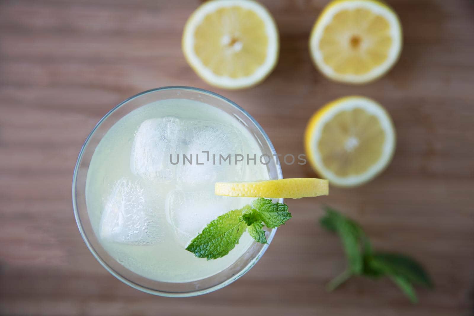 Top view of refreshing lemon drink garnished with mint and out of focus lemons on table