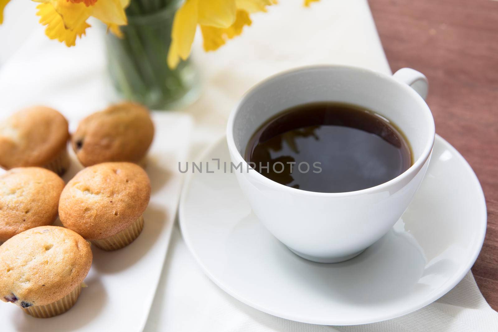 Fresh miniature blueberry muffins with coffee and spring daffodil bouquet.