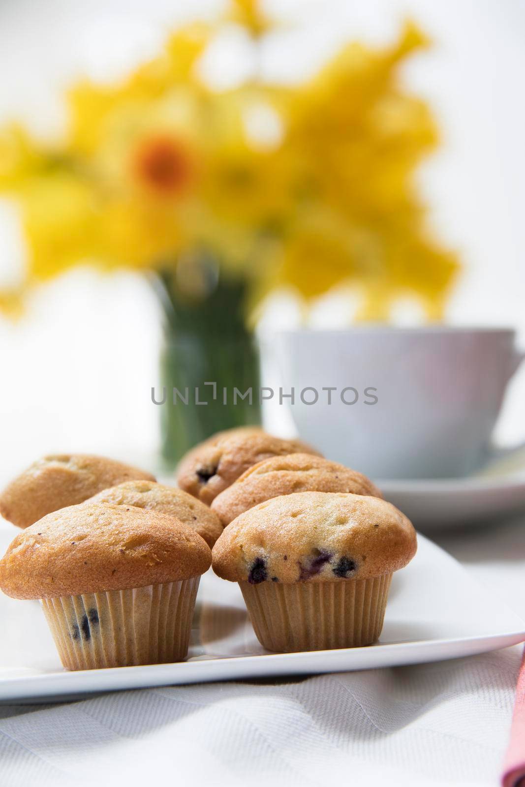 Fresh miniature blueberry muffins with coffee and spring daffodil bouquet.