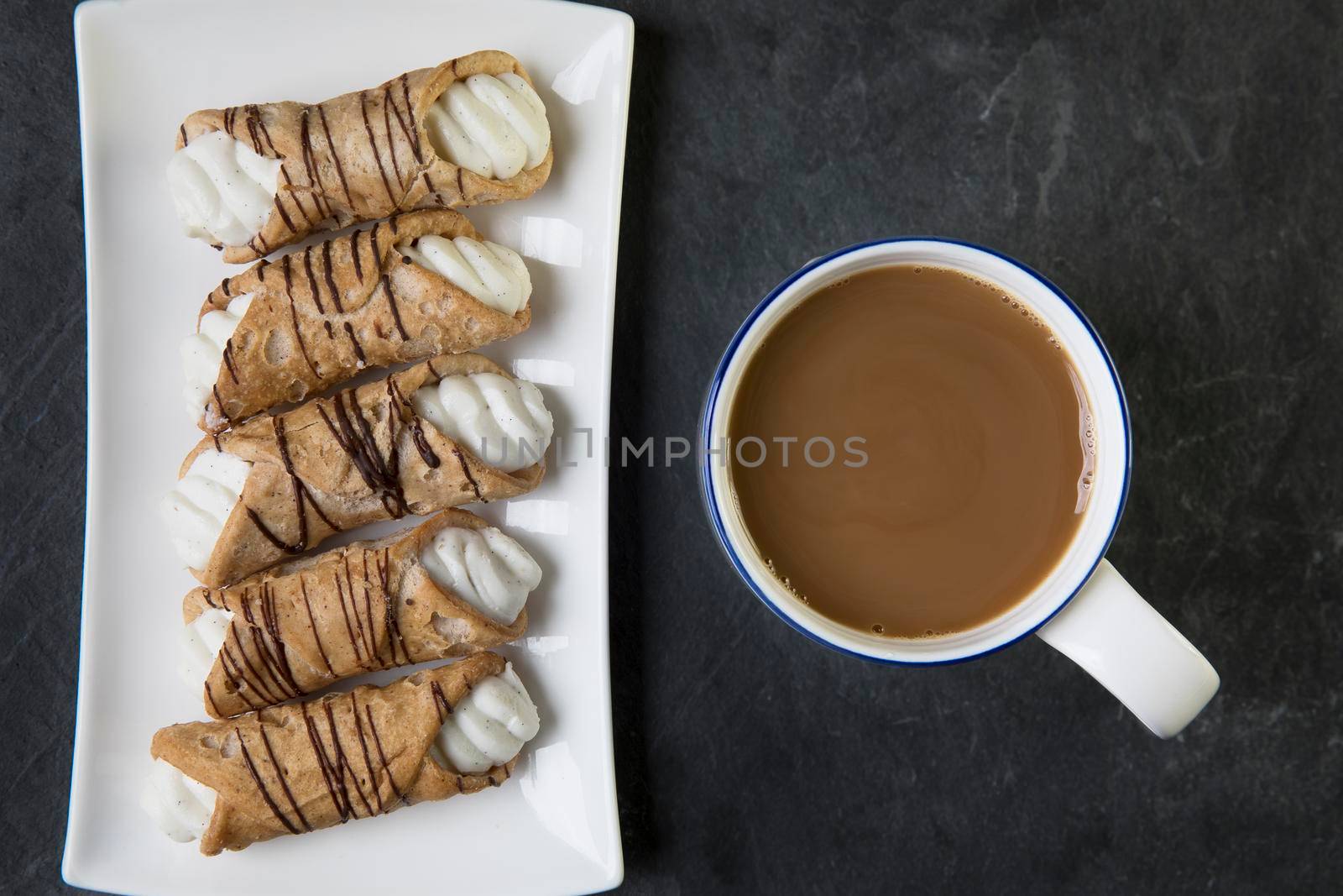 Pastries Stuffed with sweet cream and drizzled with chocolate and a cup of tea or coffee, viewed from above.