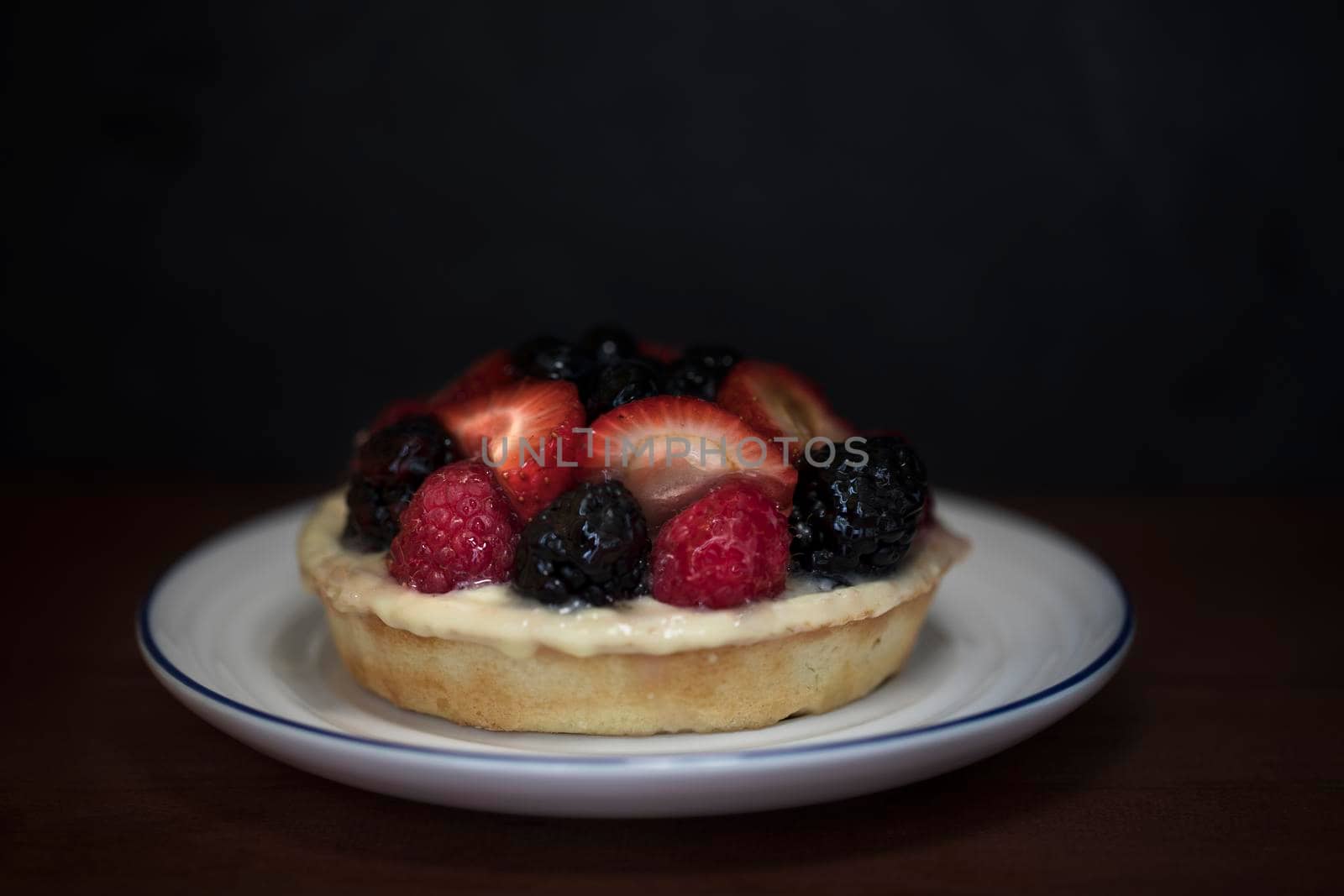 Small fruit topped cheesecake in small plate with dark background.