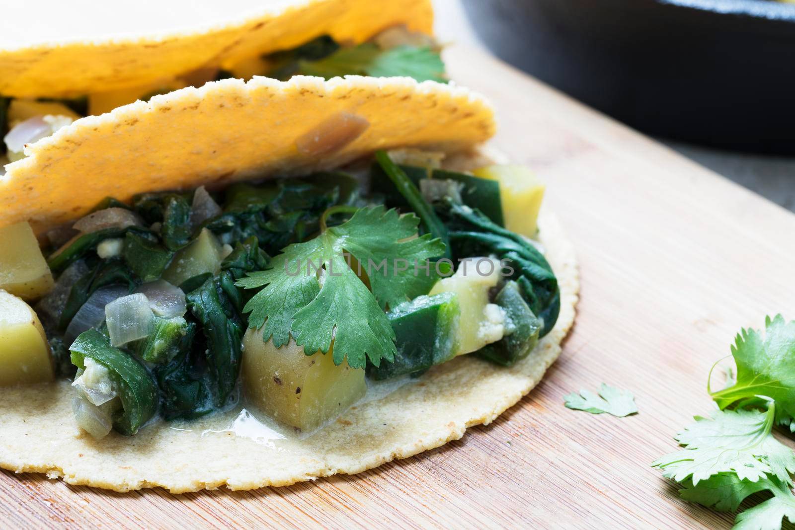 Two vegan soft tacos filled with potatoes and spinach and topped with cilantro.